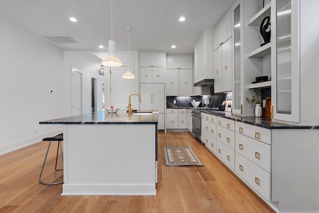 kitchen featuring hanging light fixtures, a kitchen island with sink, high end stainless steel range, white cabinets, and light wood-type flooring