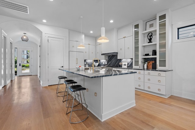 kitchen with hanging light fixtures, backsplash, dark stone countertops, white cabinets, and light wood-type flooring