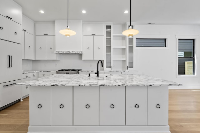 kitchen with white cabinetry, light wood-type flooring, and a center island with sink