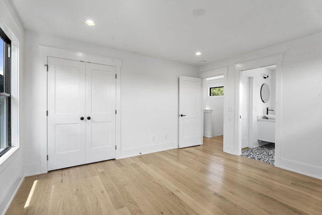 unfurnished bedroom featuring a closet, ensuite bath, and light hardwood / wood-style flooring