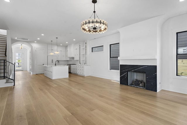 unfurnished living room featuring a notable chandelier, sink, a premium fireplace, and light wood-type flooring