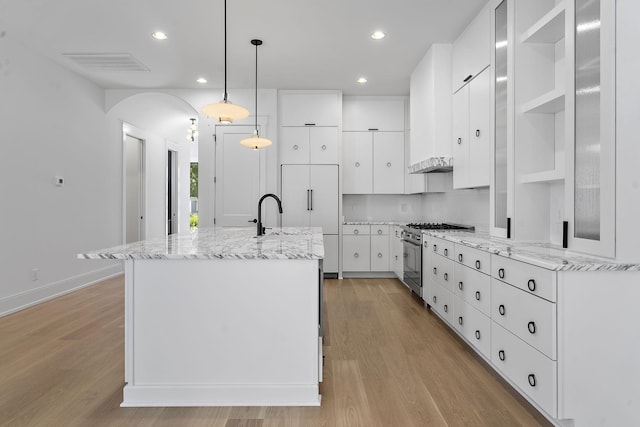 kitchen with hanging light fixtures, high quality appliances, an island with sink, light stone countertops, and white cabinets