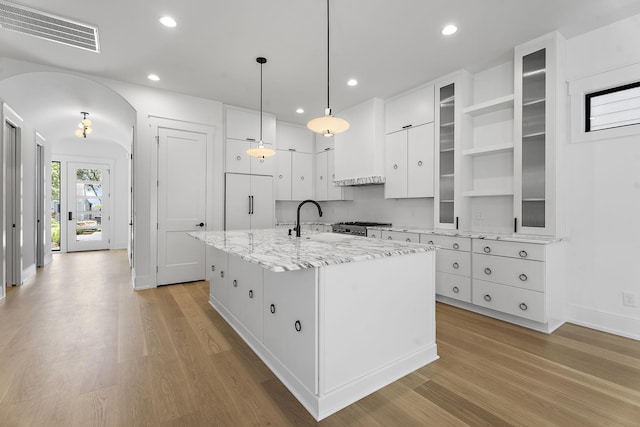 kitchen featuring a kitchen island with sink, pendant lighting, white cabinets, and light wood-type flooring