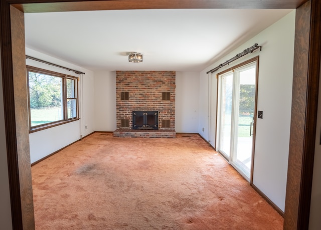 unfurnished living room with light colored carpet, a brick fireplace, and a wealth of natural light