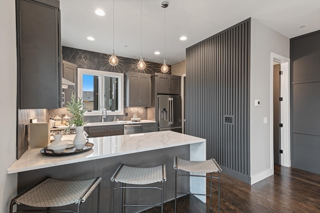 kitchen with sink, dark wood-type flooring, stainless steel appliances, tasteful backsplash, and pendant lighting