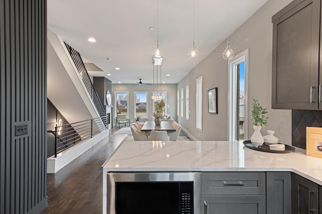 kitchen with gray cabinetry, light stone countertops, ceiling fan, hanging light fixtures, and dark hardwood / wood-style flooring