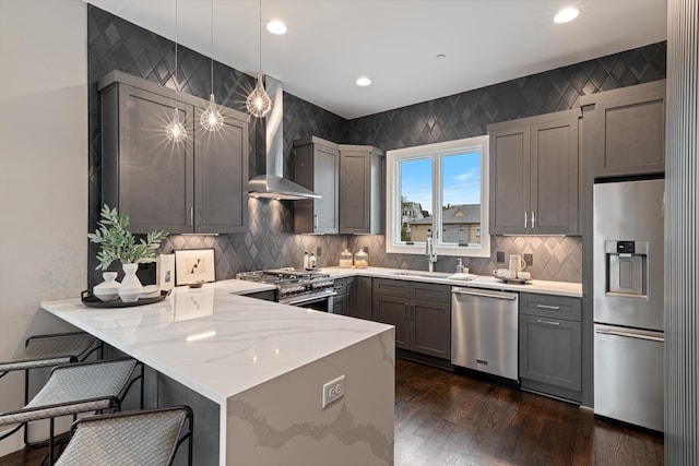 kitchen with kitchen peninsula, appliances with stainless steel finishes, wall chimney exhaust hood, sink, and hanging light fixtures