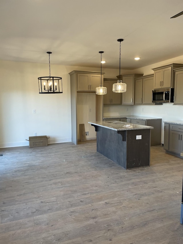 kitchen featuring gray cabinetry, hanging light fixtures, light stone countertops, a kitchen island, and light wood-type flooring