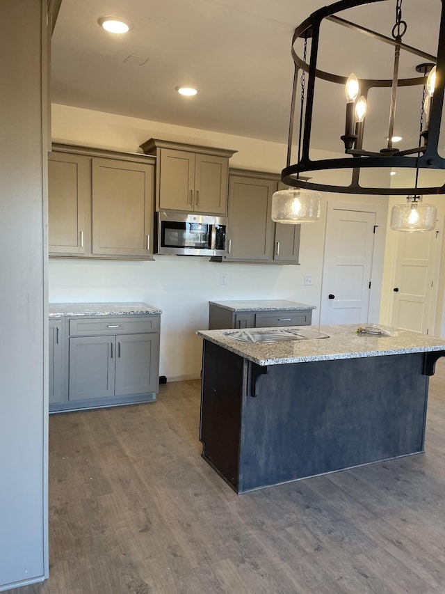 kitchen with light stone counters, decorative light fixtures, a kitchen breakfast bar, gray cabinets, and hardwood / wood-style flooring