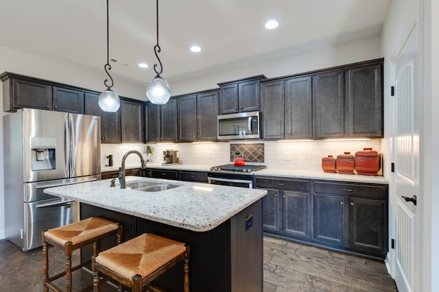 kitchen featuring light stone countertops, stainless steel appliances, a kitchen island with sink, sink, and decorative light fixtures