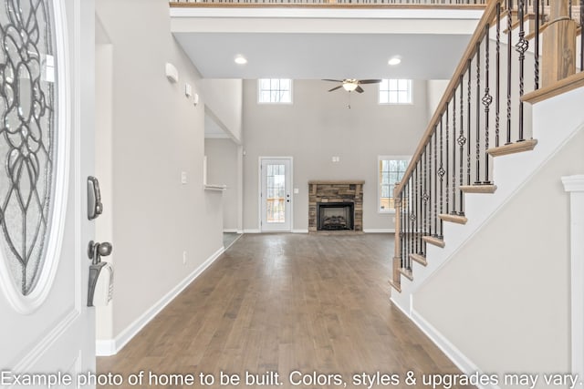 entrance foyer with ceiling fan, a towering ceiling, a fireplace, and hardwood / wood-style flooring