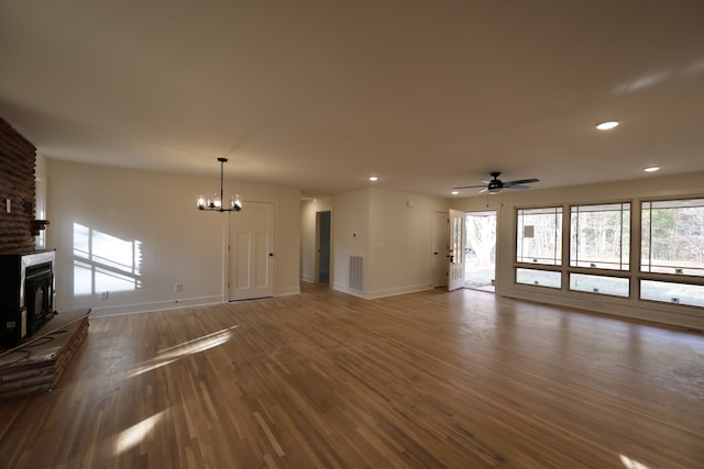 unfurnished living room featuring a large fireplace, hardwood / wood-style floors, and ceiling fan with notable chandelier