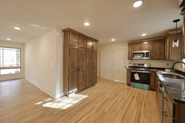 kitchen with sink, hanging light fixtures, dark stone countertops, light wood-type flooring, and stainless steel appliances