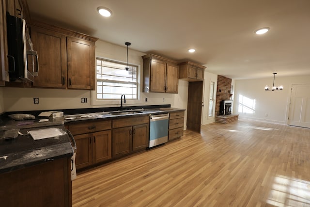 kitchen featuring sink, a brick fireplace, light wood-type flooring, decorative light fixtures, and stainless steel appliances