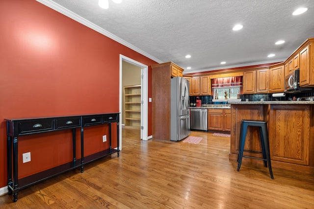 kitchen with a kitchen bar, appliances with stainless steel finishes, kitchen peninsula, light stone countertops, and light hardwood / wood-style floors