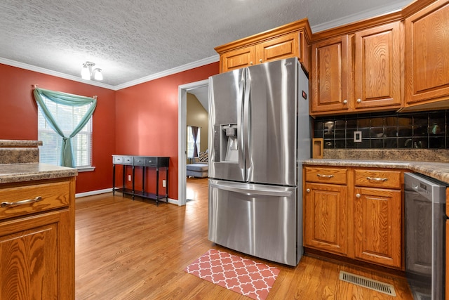 kitchen with stainless steel appliances, backsplash, crown molding, a textured ceiling, and light wood-type flooring