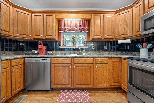 kitchen featuring backsplash, sink, stainless steel appliances, and light hardwood / wood-style flooring