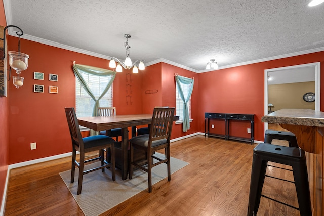 dining space featuring a textured ceiling, hardwood / wood-style flooring, ornamental molding, and a notable chandelier