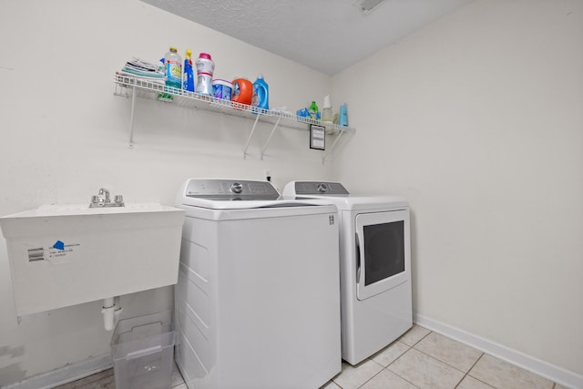 clothes washing area featuring a textured ceiling, separate washer and dryer, sink, and light tile patterned floors