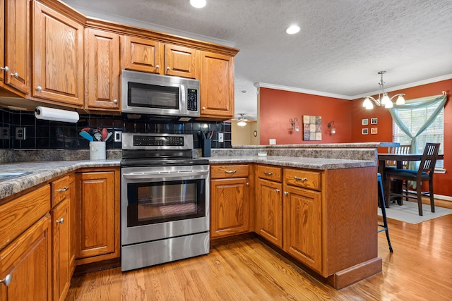 kitchen featuring light wood-type flooring, ornamental molding, tasteful backsplash, kitchen peninsula, and stainless steel appliances