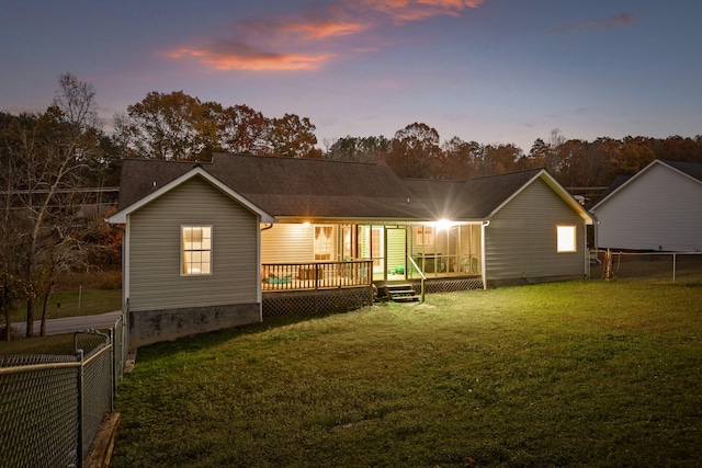 back house at dusk featuring a wooden deck and a yard