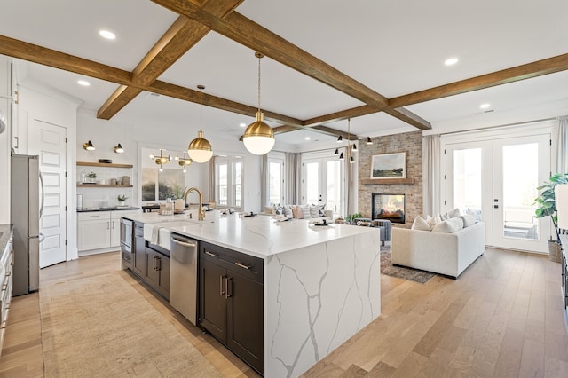 kitchen featuring light stone countertops, stainless steel appliances, a kitchen island with sink, pendant lighting, and light hardwood / wood-style flooring