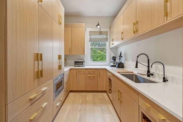 kitchen with light brown cabinets, light stone counters, light wood-type flooring, and sink