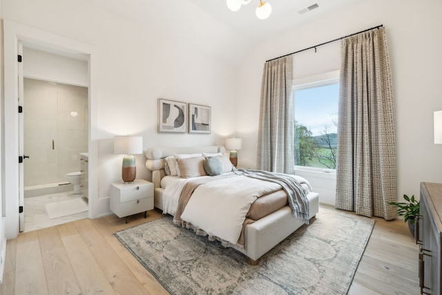 bedroom featuring light hardwood / wood-style floors, lofted ceiling, and connected bathroom