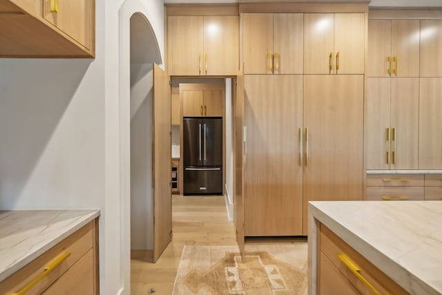 kitchen featuring light stone countertops, high end refrigerator, light brown cabinets, and light hardwood / wood-style floors