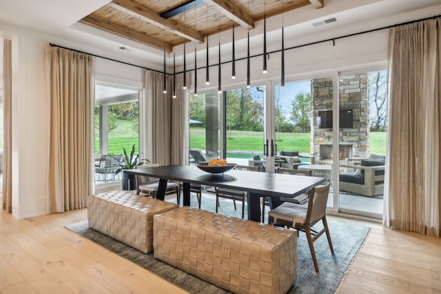 dining area with beam ceiling, a stone fireplace, wood ceiling, and light hardwood / wood-style flooring