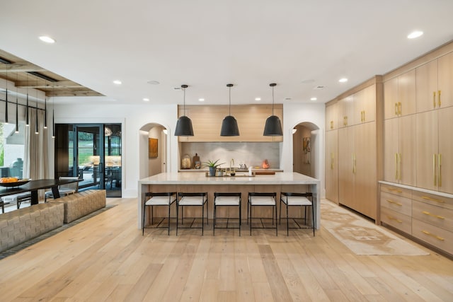 kitchen with light brown cabinetry, light hardwood / wood-style flooring, pendant lighting, and a large island