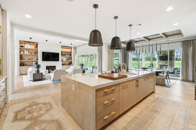 kitchen featuring pendant lighting, light brown cabinets, light hardwood / wood-style flooring, and a kitchen island with sink