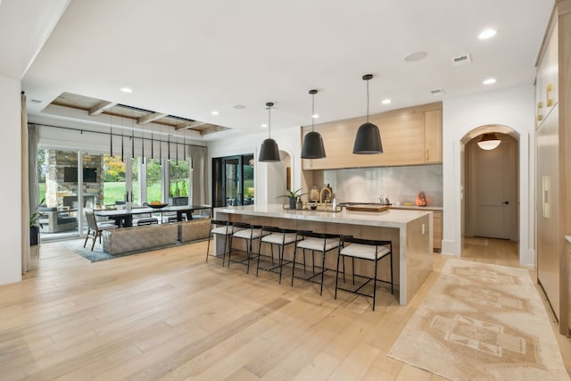 kitchen with light brown cabinetry, a kitchen island with sink, light hardwood / wood-style floors, hanging light fixtures, and a breakfast bar area