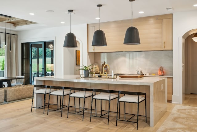 kitchen with light hardwood / wood-style floors, decorative light fixtures, a breakfast bar area, decorative backsplash, and light brown cabinetry