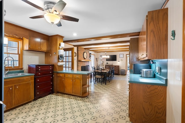 kitchen with kitchen peninsula, ceiling fan, sink, and beamed ceiling