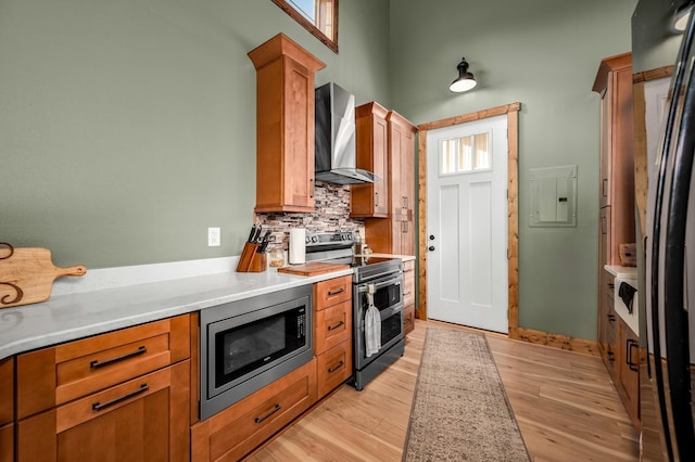 kitchen with appliances with stainless steel finishes, backsplash, light hardwood / wood-style floors, and wall chimney exhaust hood