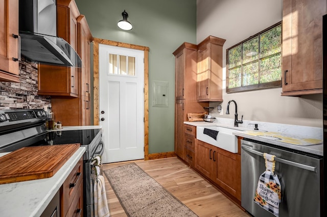 kitchen featuring sink, wall chimney exhaust hood, light stone countertops, light wood-type flooring, and stainless steel appliances