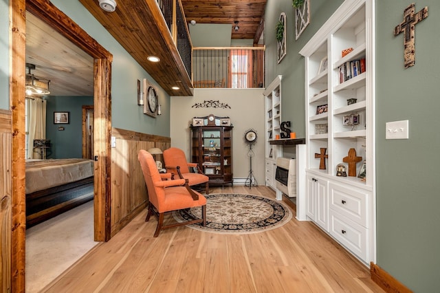 living area featuring a towering ceiling, light wood-type flooring, wooden ceiling, and wood walls