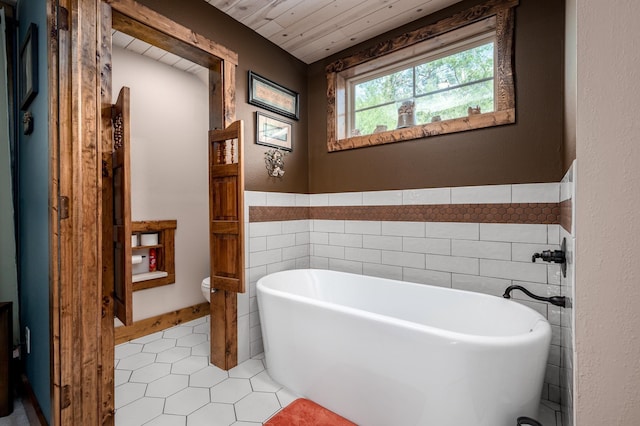 bathroom featuring a bathing tub, tile patterned floors, toilet, wood ceiling, and tile walls