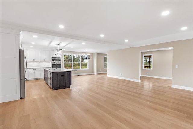 kitchen featuring a kitchen island with sink, sink, decorative light fixtures, light hardwood / wood-style floors, and stainless steel refrigerator