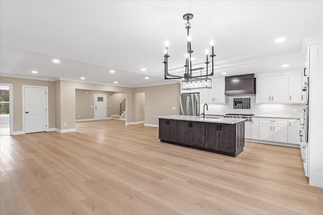 kitchen with light hardwood / wood-style flooring, wall chimney range hood, stainless steel appliances, and an island with sink