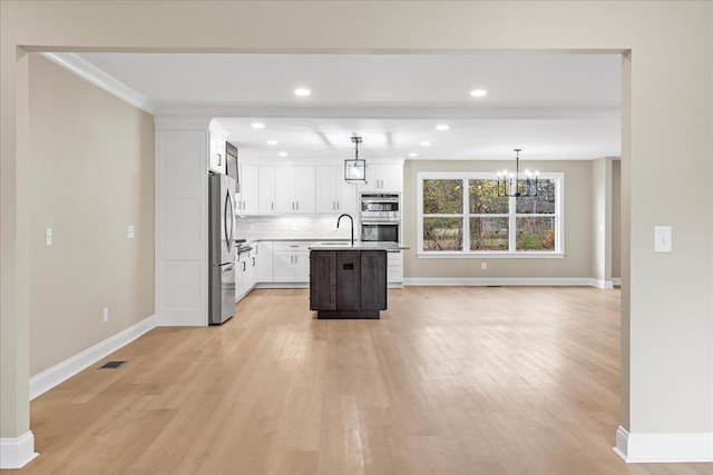 kitchen with a kitchen island with sink, white cabinets, light wood-type flooring, appliances with stainless steel finishes, and decorative light fixtures