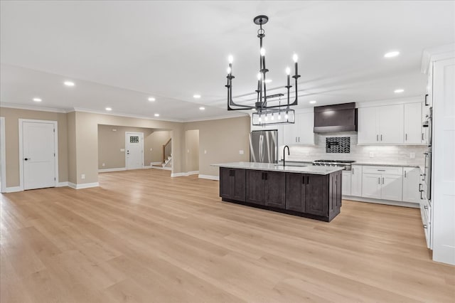 kitchen featuring stainless steel appliances, wall chimney range hood, light hardwood / wood-style flooring, pendant lighting, and a center island with sink