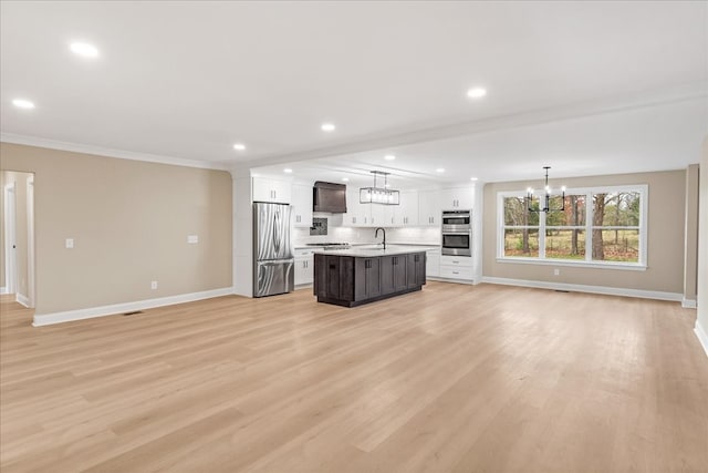 kitchen featuring a kitchen island with sink, wall chimney range hood, stainless steel appliances, and hanging light fixtures