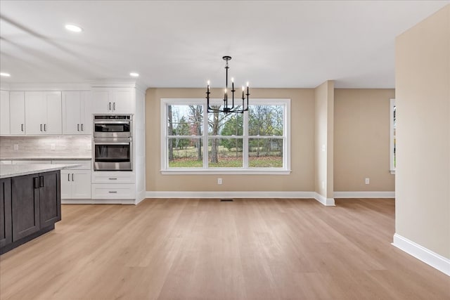 kitchen with hanging light fixtures, stainless steel double oven, a notable chandelier, light hardwood / wood-style floors, and white cabinets