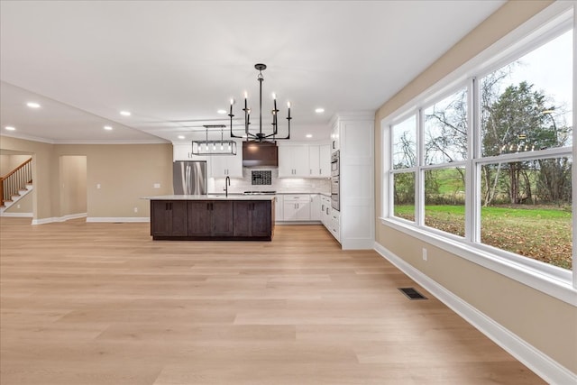 kitchen featuring white cabinets, stainless steel fridge, light hardwood / wood-style floors, and a kitchen island with sink