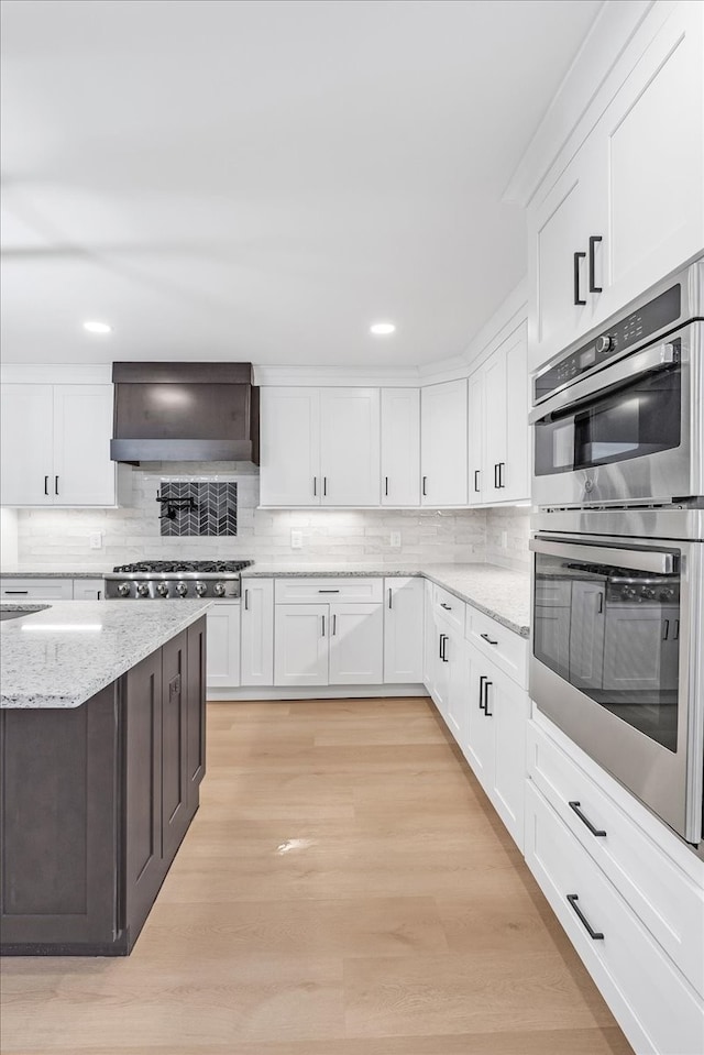 kitchen with custom range hood, light wood-type flooring, stainless steel appliances, and white cabinetry