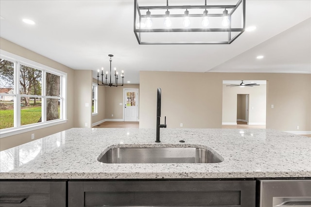 kitchen featuring light stone counters, ceiling fan with notable chandelier, sink, wood-type flooring, and pendant lighting