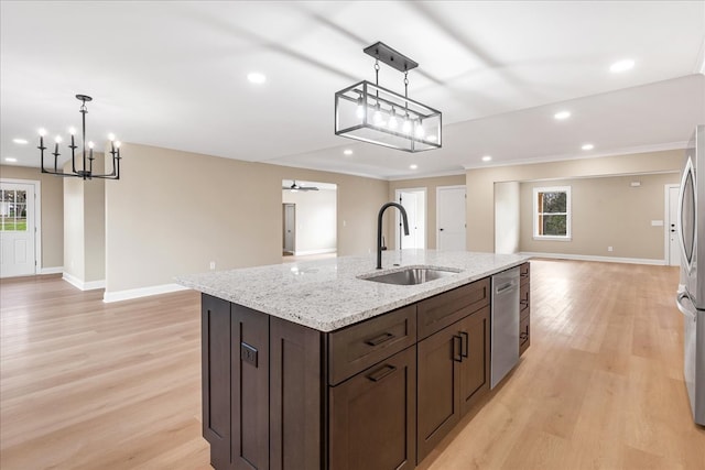 kitchen featuring appliances with stainless steel finishes, ceiling fan with notable chandelier, sink, light hardwood / wood-style flooring, and an island with sink