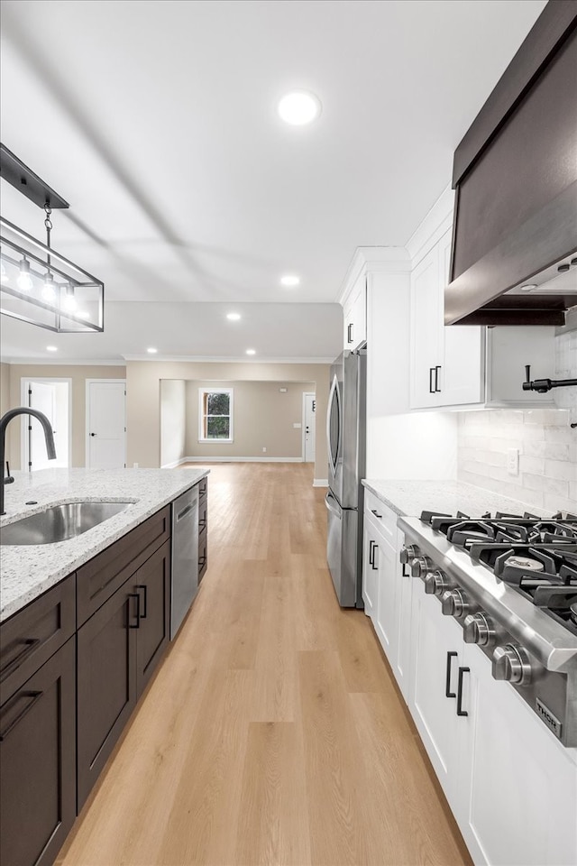 kitchen featuring sink, wall chimney exhaust hood, light wood-type flooring, appliances with stainless steel finishes, and white cabinetry